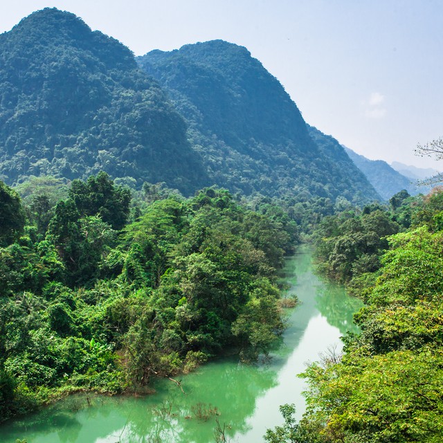 A lush green jungle with a steep mountain and river running through it.